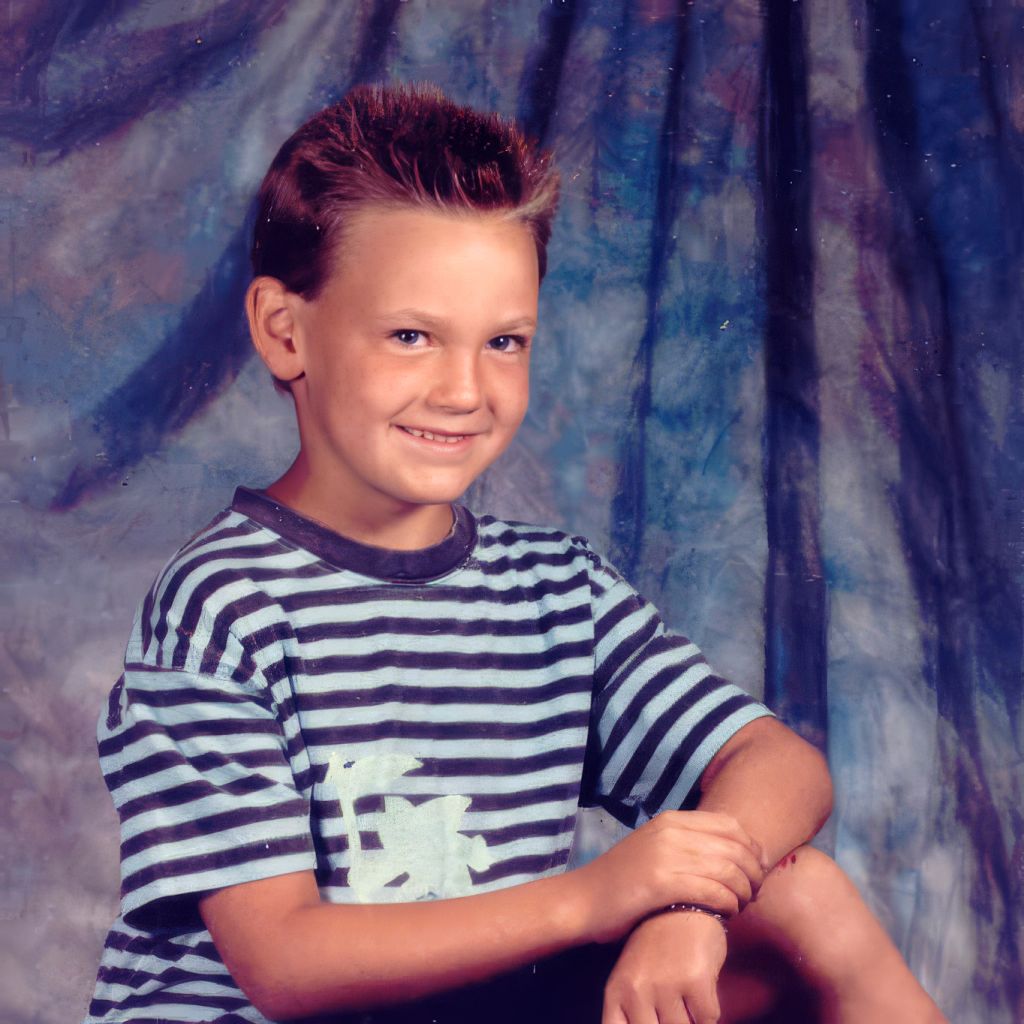 A school portrait of Sean as a boy in a striped shirt against a painted studio backdrop. The image marks the earliest point on the path — long before the work had a name, when the questions were already forming.
